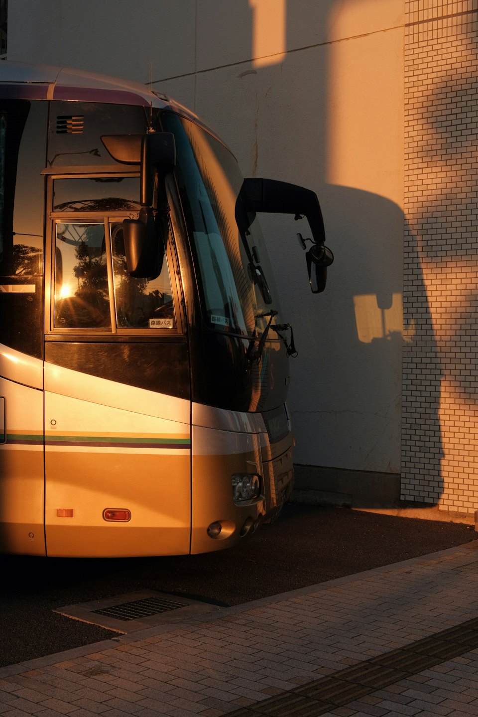 Beige och grå buss parkerad vid en tegelvägg i solnedgången.